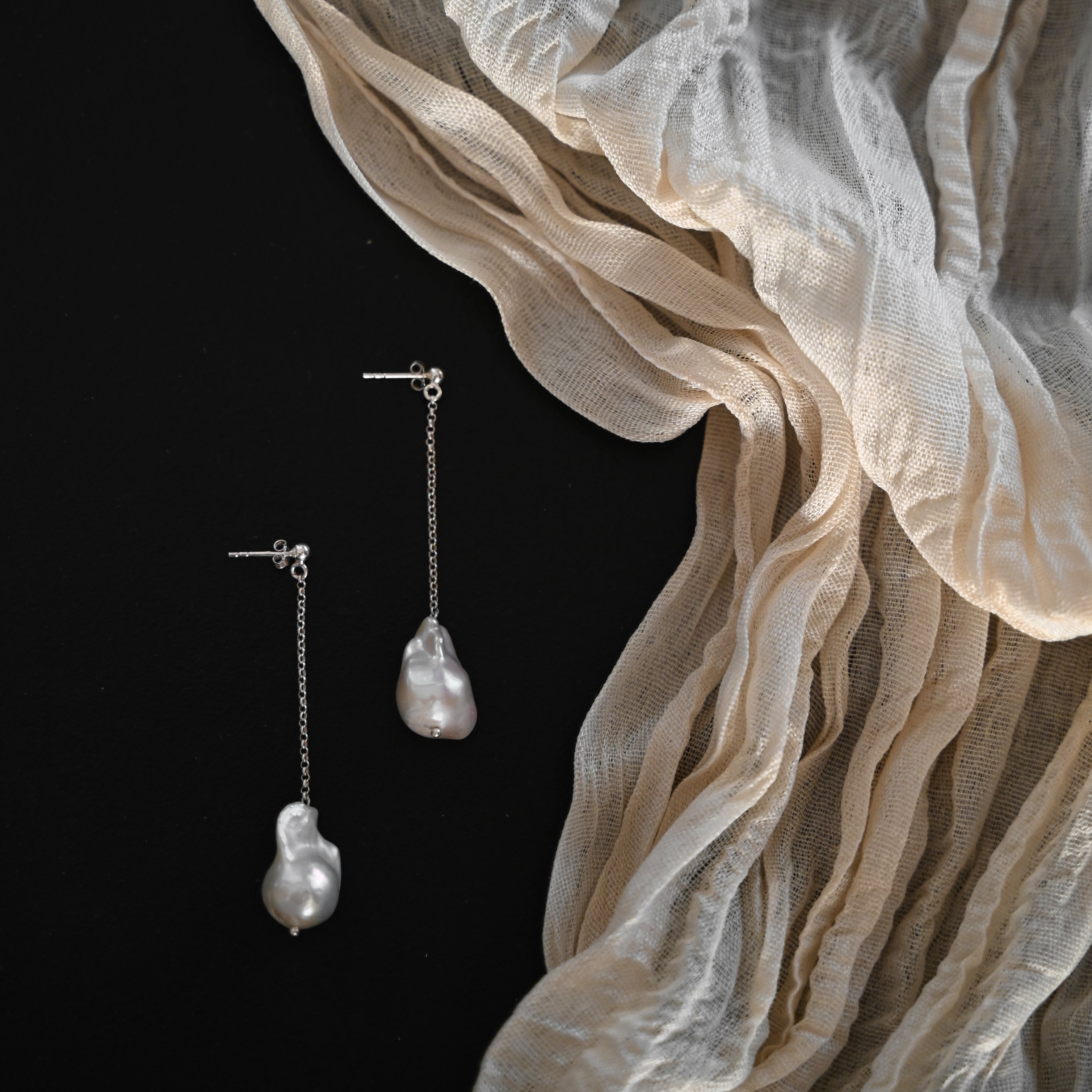 Pearl earrings on a black background with beige fabric