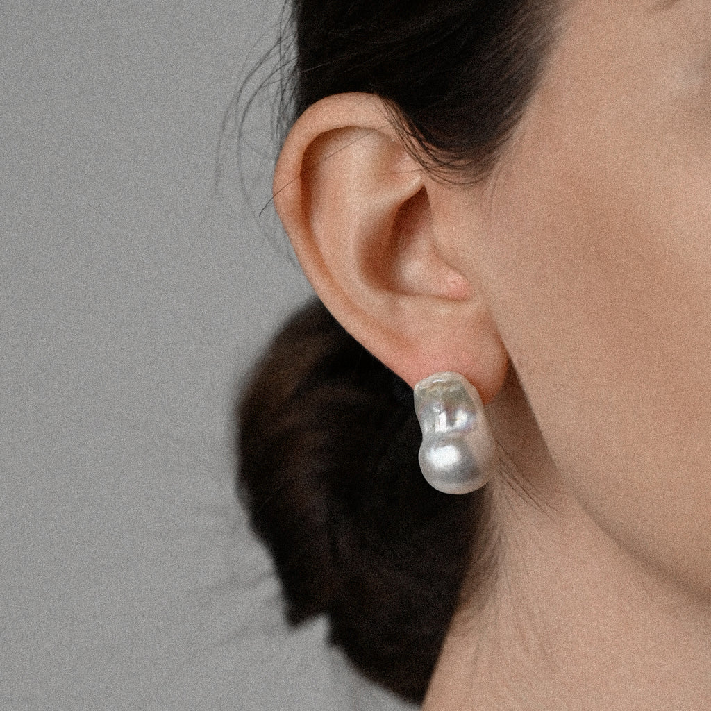 Close-up of an ear wearing a pearl earring against a neutral background