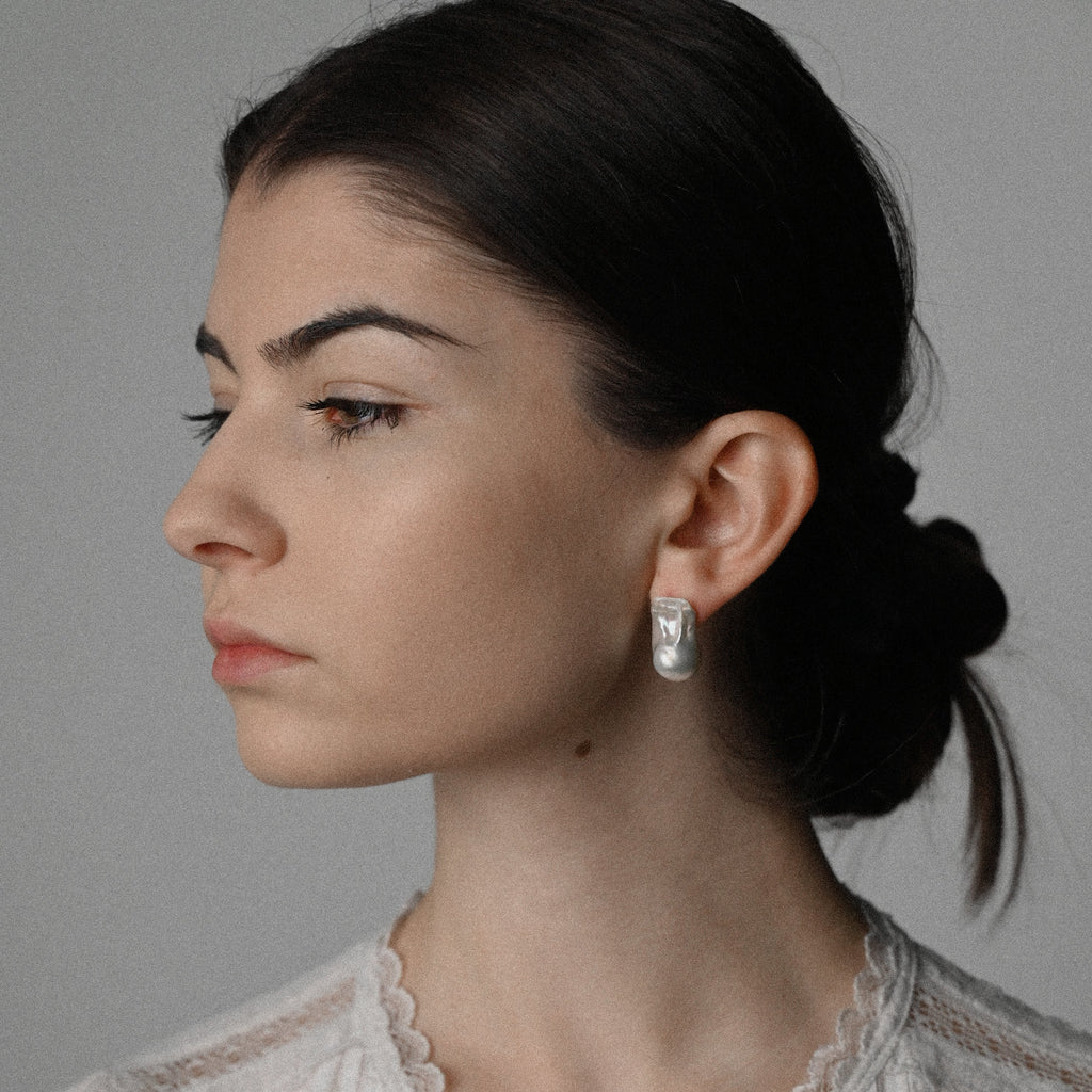 Woman wearing a silver baroque pearl earring against a neutral background
