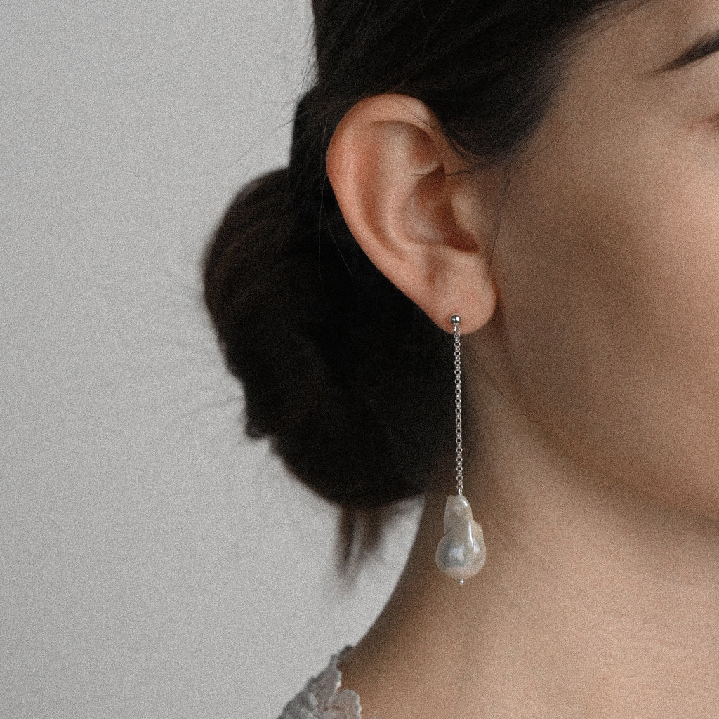 Woman wearng long white pearl earrings against a white background