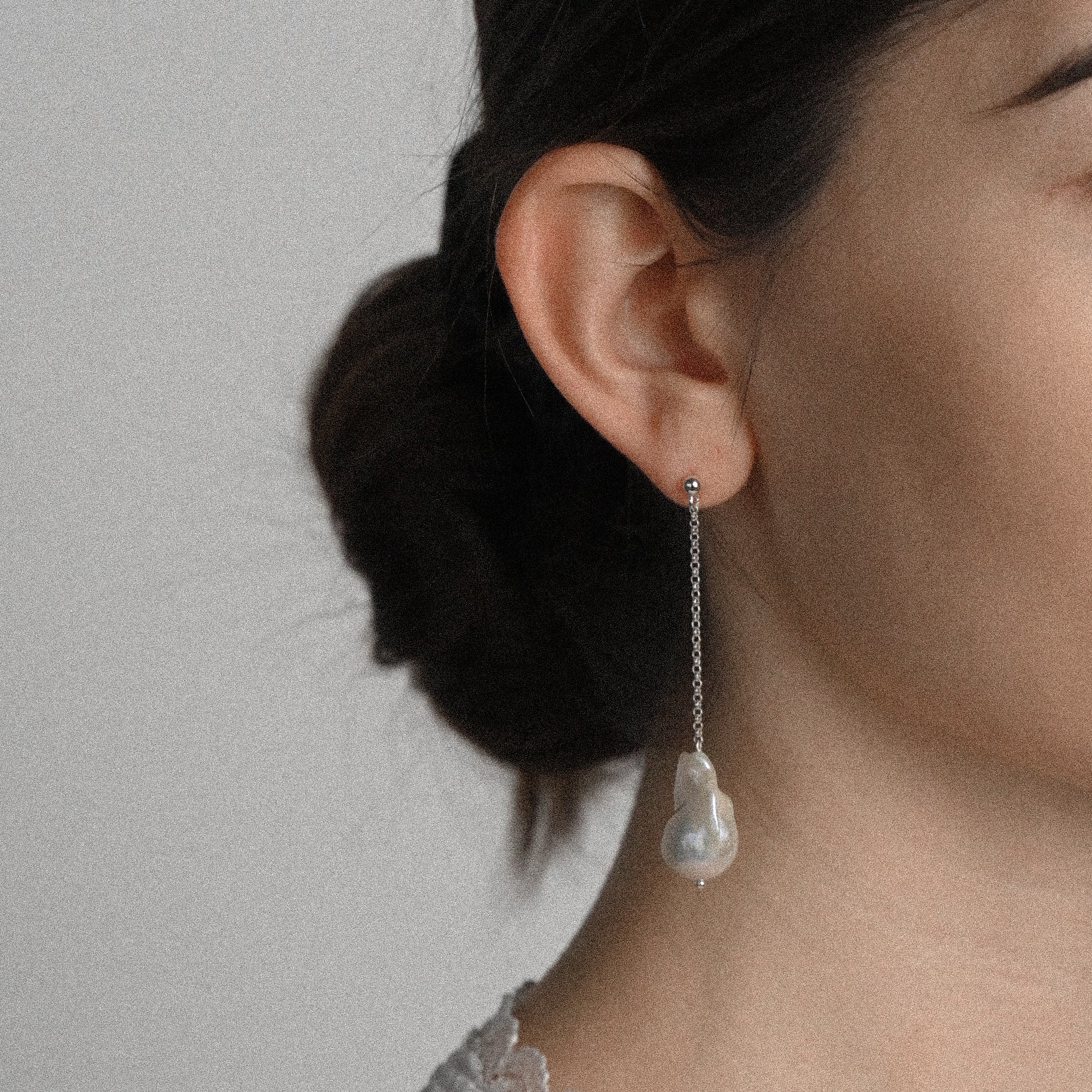 Woman wearng long white pearl earrings against a white background