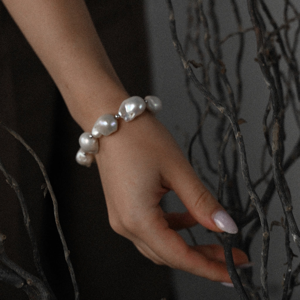 Hand wearing a natural baroque pearl bracelet with a dark background