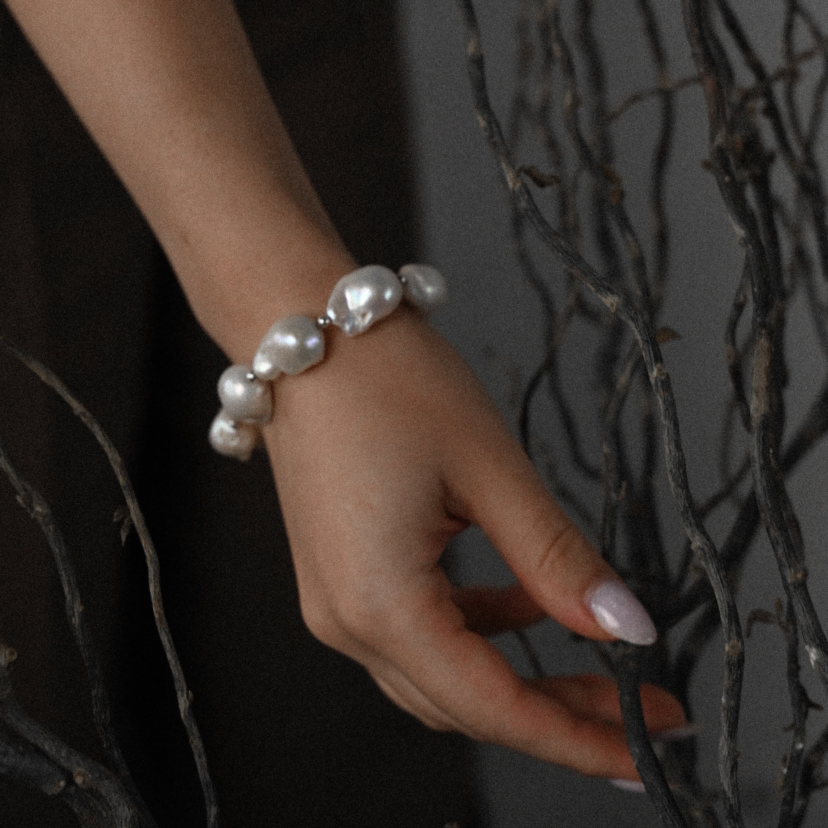 Hand wearing a natural baroque pearl bracelet with a dark background