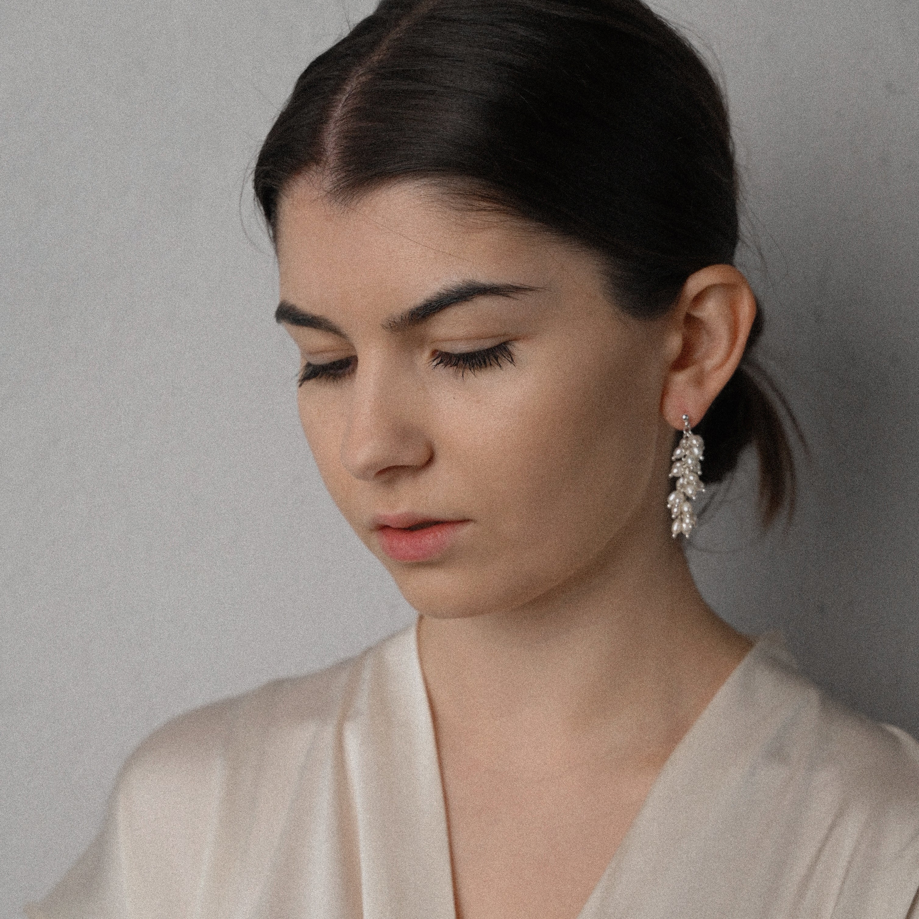 Woman wearing a beige top and white pearl silver earrings against a plain background