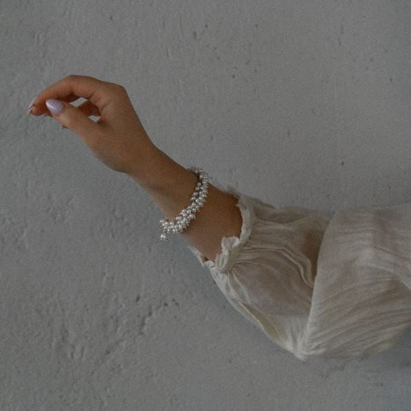 Hand wearing a white pearl silver bracelet against a plain background