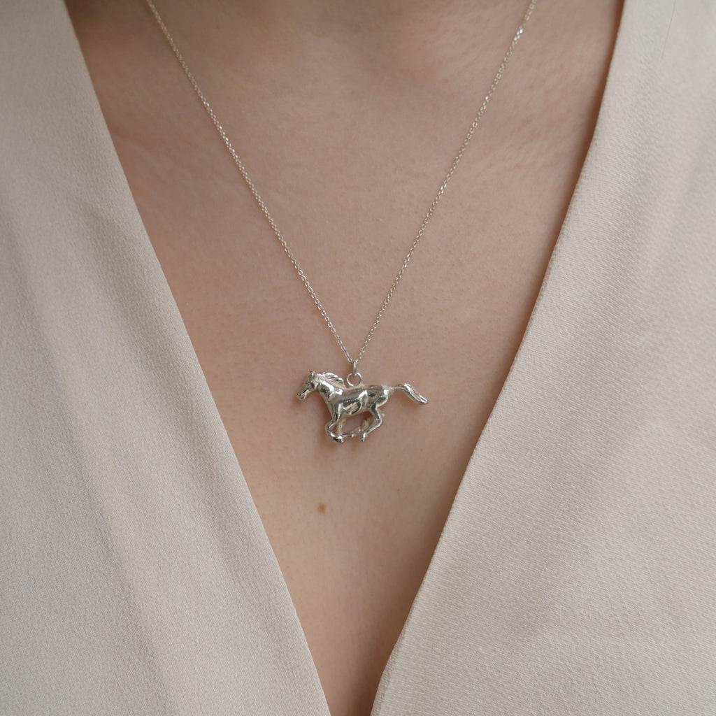 Silver horse pendant necklace on a person wearing a beige top