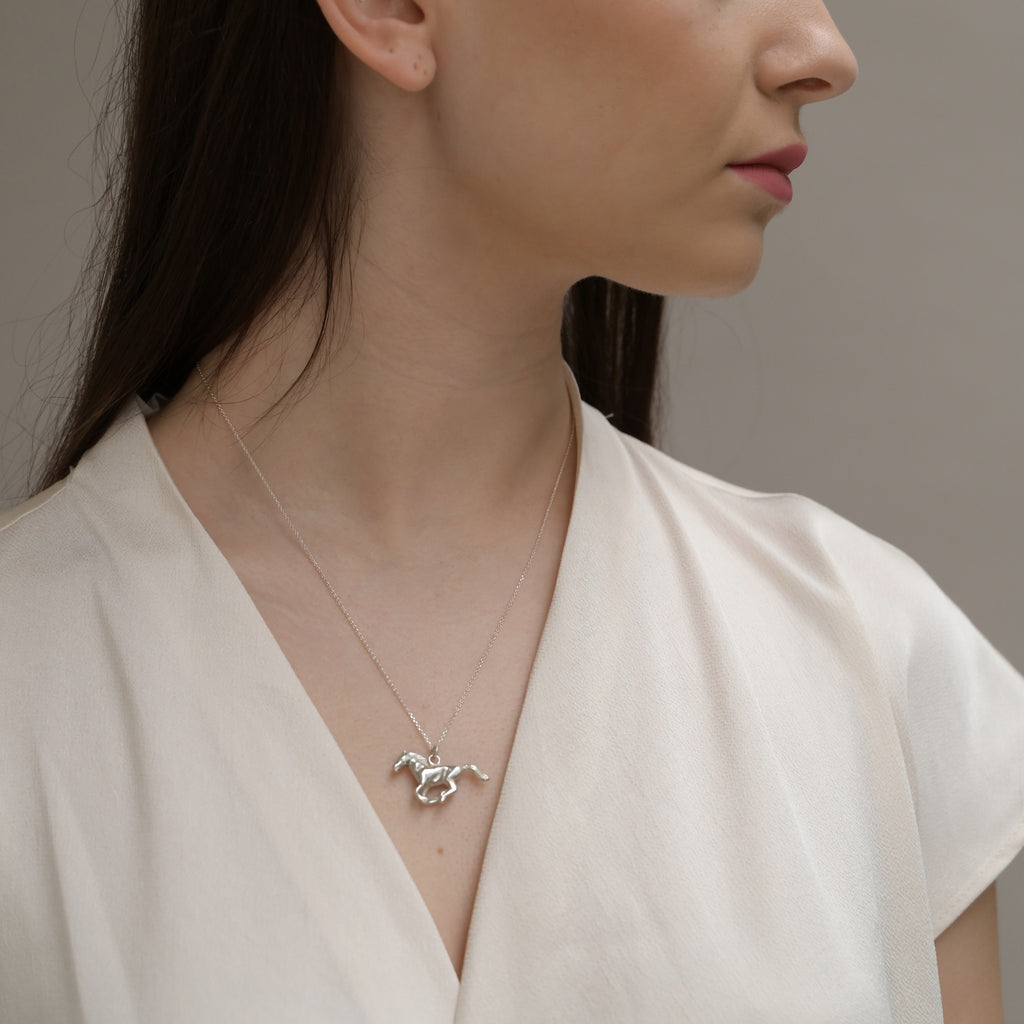 Woman wearing a silver necklace with a horse pendant against a neutral background