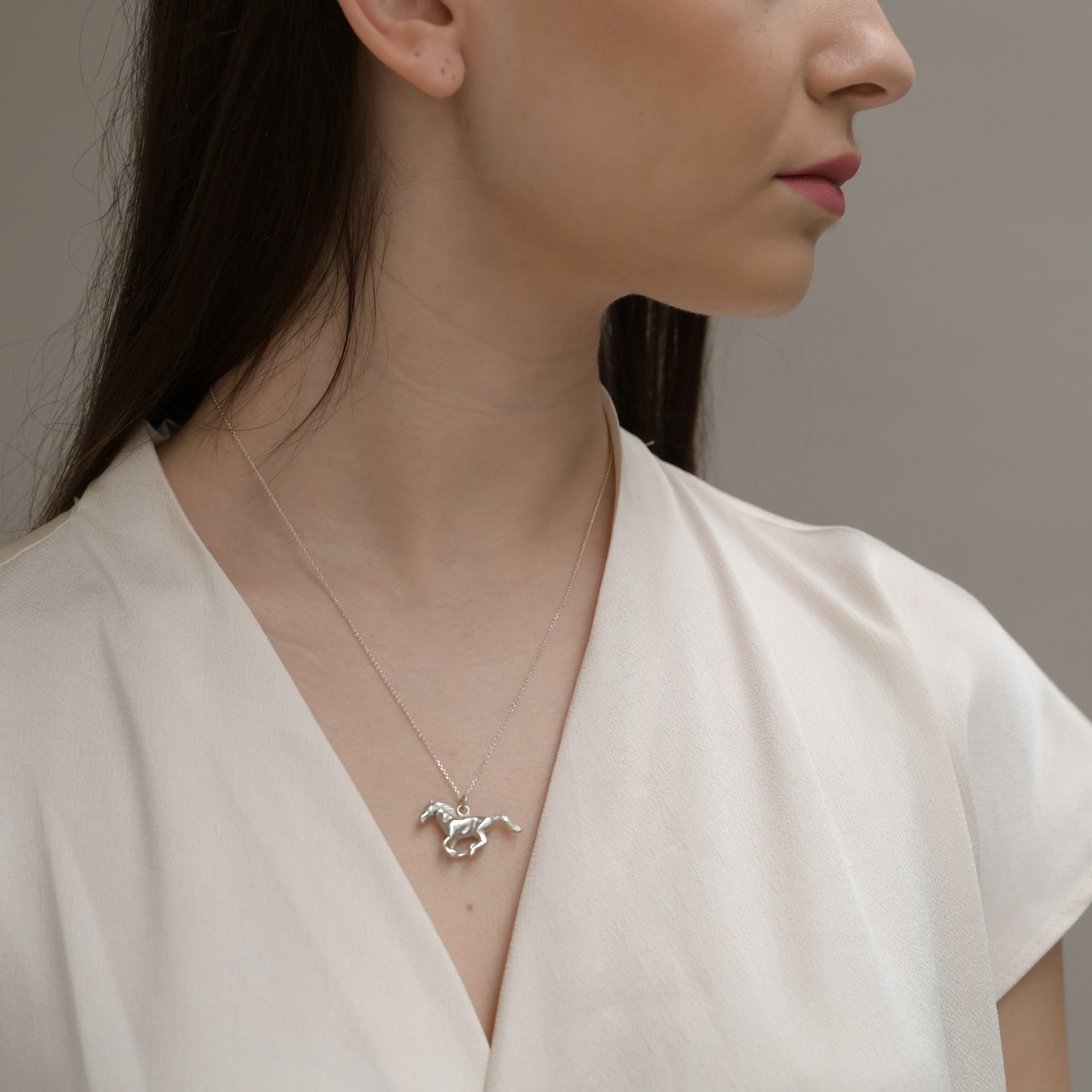 Woman wearing a silver necklace with a horse pendant against a neutral background