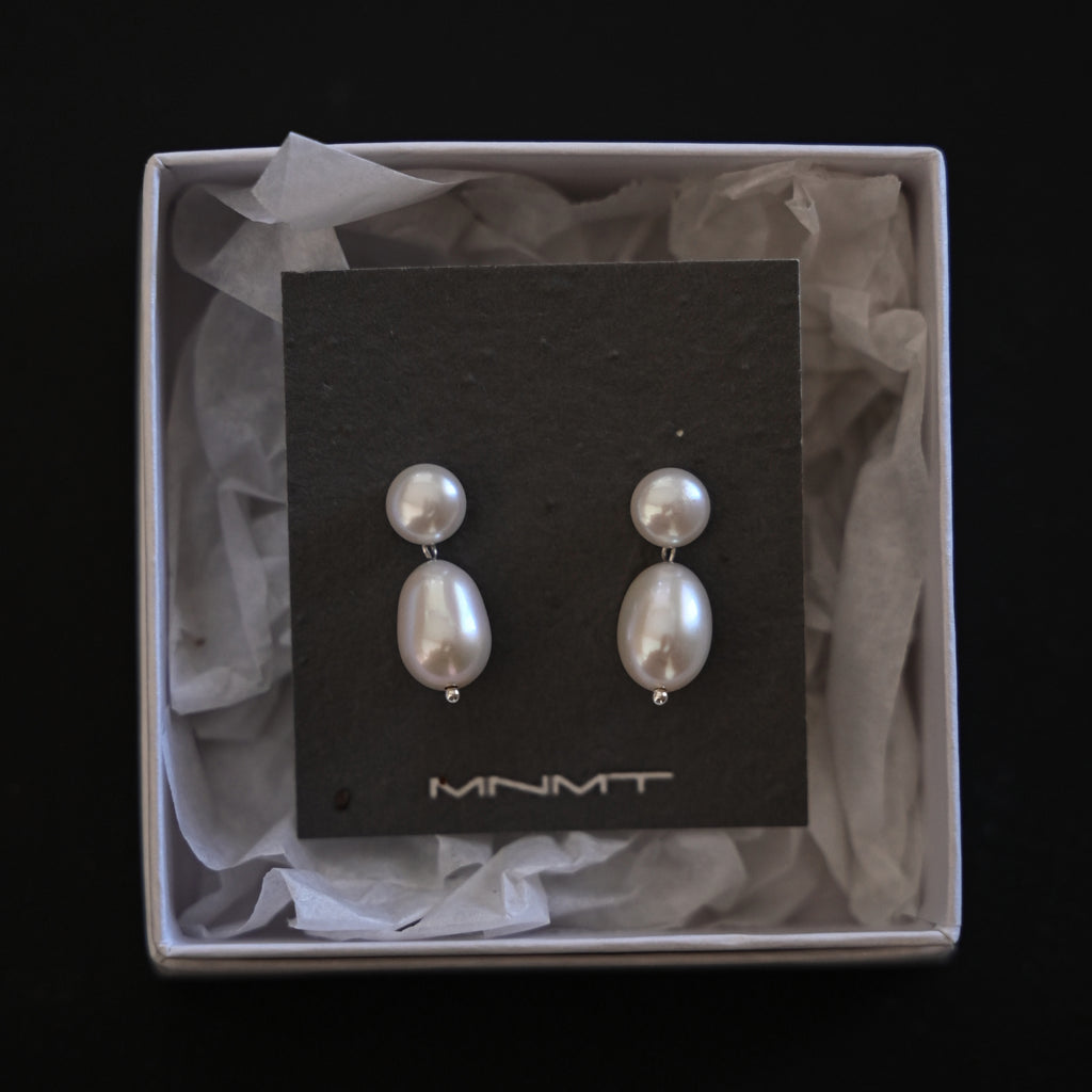 Pair of pearl earrings on a black card with 'MNMT' branding, displayed in a box.
