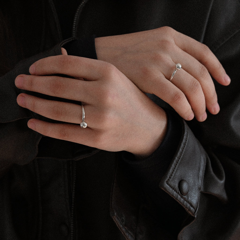 Hands with sterling silver minimalist rings on a dark background
