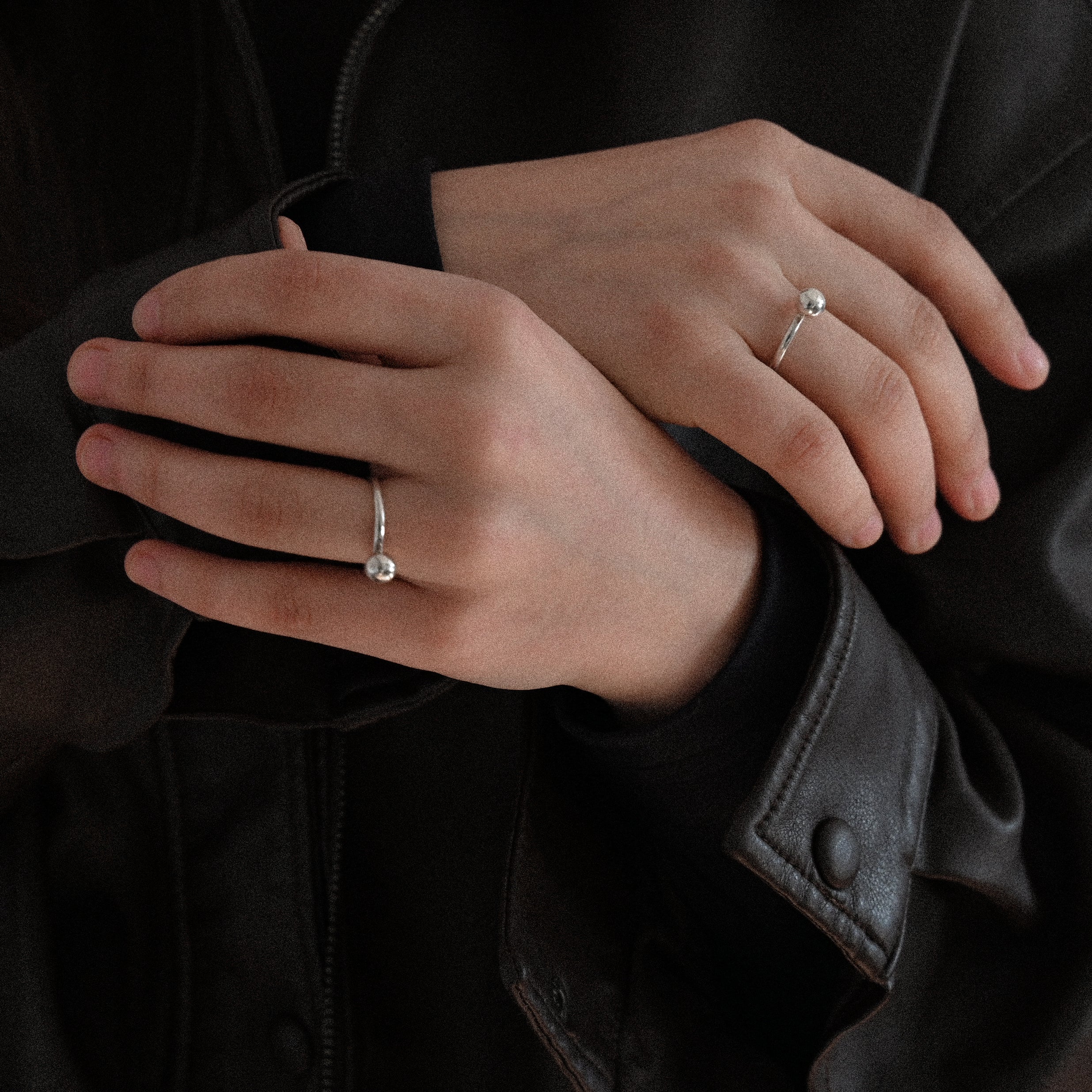 Hands with sterling silver minimalist rings on a dark background