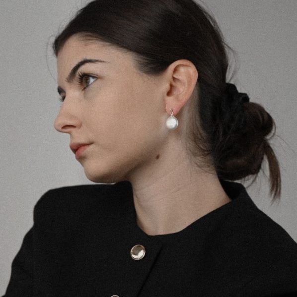 Woman wearing white pearl silver earrings against a neutral background